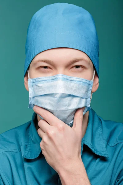 Mannelijke chirurg in masker camera kijken op blauwe achtergrond, close-up — Stockfoto