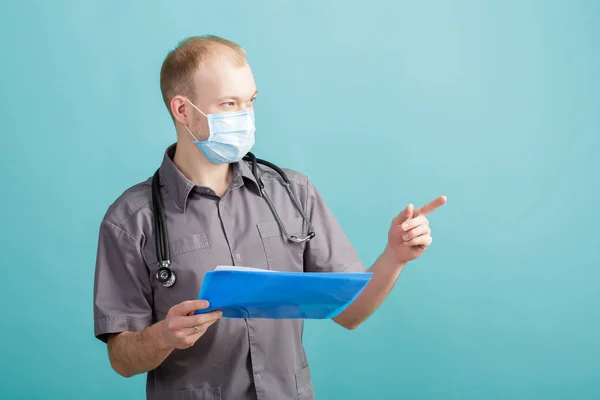 Jonge mannelijke arts houden een map met papieren op blauwe achtergrond — Stockfoto