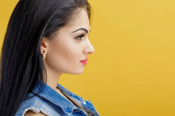 Portret van aantrekkelijke jonge brunette vrouw in denim vest op gele achtergrond. — Stockfoto