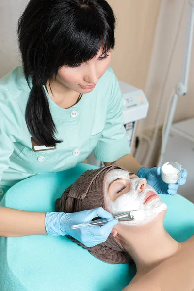 Косметолог надевает маску на красивую молодую женщину в Спа салоне. косметическая процедура уход за кожей. Микродермабразия — стоковое фото
