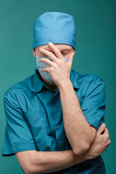 Moe mannelijke chirurg in masker op blauwe achtergrond, close-up — Stockfoto