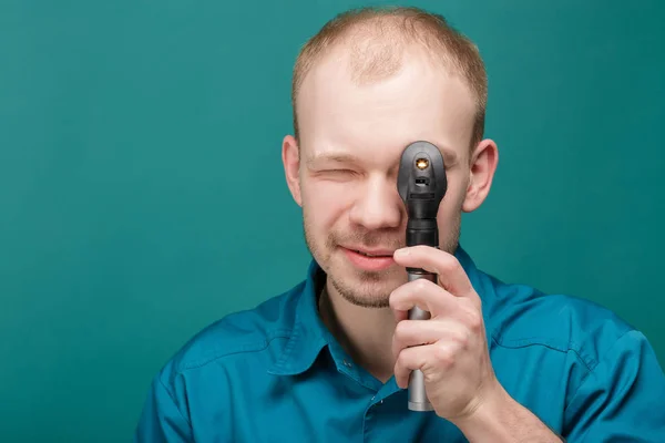 Optometrista con oftalmoscopio, strumento per guardare negli occhi dal medico su sfondo blu — Foto Stock