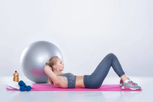 Vacker blond flicka i sportkläder gör övningar på fitness Mat på grå bakgrund — Stockfoto