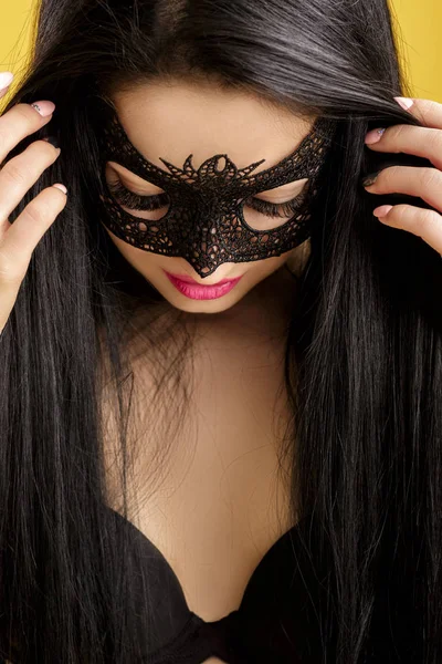 Retrato de bela mulher sensual em máscara de renda preta no fundo amarelo. menina sexy em máscara veneziana — Fotografia de Stock