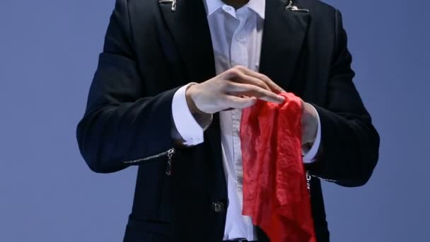 Фокусник показує трюк з червоним шарфом на темному тлі — стокове відео