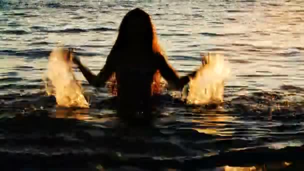물으로 튀기를 만드는 여자의 실루엣입니다. 바다에서 휴가 여행. — 비디오