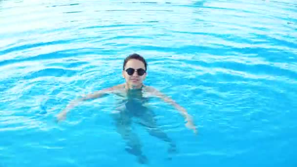 Joven morena en bikini y gafas de sol nada en la piscina el soleado día de verano — Vídeo de stock