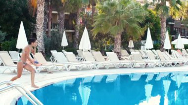bikinili genç esmer kadın güneşli yaz gününde havuz içine atlar. ağır çekim