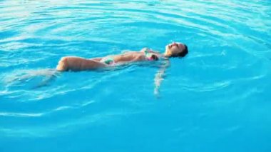 bikini ve güneş gözlüğü genç esmer kadın havuzda güneşli yaz gününde yüzüyor.