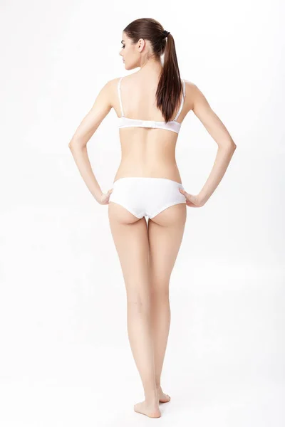 Vista trasera de hermosa joven morena con cuerpo deportivo perfecto en lencería blanca sobre fondo blanco . — Foto de Stock