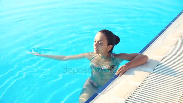 Молодая брюнетка в бикини в бассейне в солнечный летний день — стоковое видео