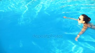 bikini ve güneş gözlüğü genç esmer kadın havuzda güneşli yaz gününde yüzüyor.