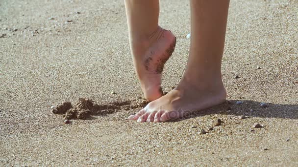 Загорелые женские ноги на пляже. вода брызгает на ноги в океане на песчаном пляже — стоковое видео