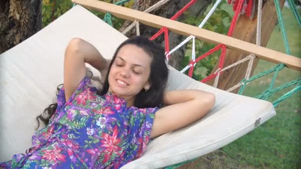 Femme brune souriante en chapeau détendu et rêvant dans l'hamac sur la plage tropicale — Video