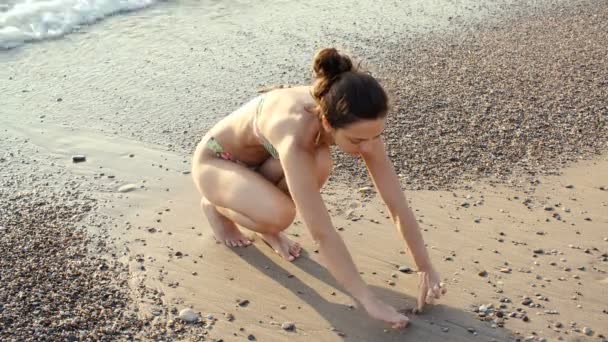 Молодая женщина черпает сердце в песке на берегу моря в солнечный день — стоковое видео