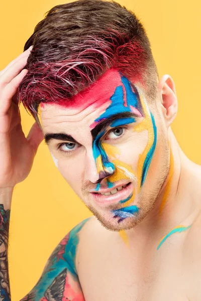 Portret van een jonge man met gekleurde gezicht schilderen op gele achtergrond. Professionele make-up mode. fantasy art make-up — Stockfoto
