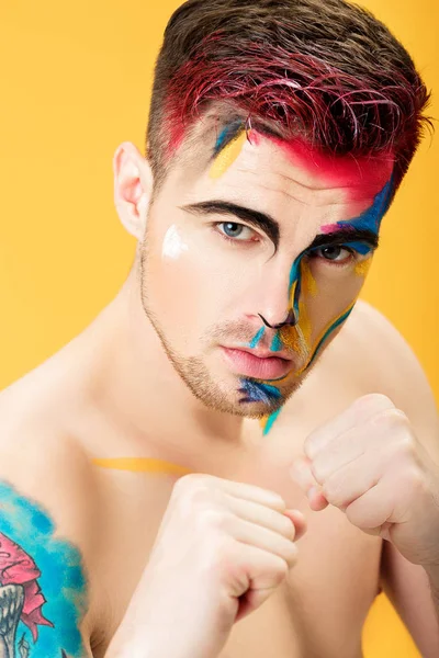 Retrato de hombre joven con pintura facial de color sobre fondo amarillo. Moda de maquillaje profesional. fantasía arte maquillaje — Foto de Stock