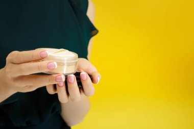 female hands holding face powder on yellow background clipart