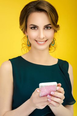 güzel gülümseyen kız smartphone üzerinde sarı arka plan kullanır.