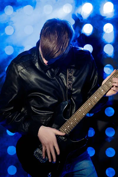 Jovem músico de rock tocando guitarra elétrica e cantando. Estrela de rock no fundo dos holofotes — Fotografia de Stock
