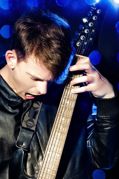 Jovem músico de rock atraente tocando guitarra elétrica e cantando. Estrela de rock no fundo dos holofotes — Fotografia de Stock