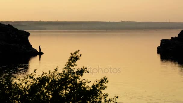 Silueta de un pescador pescando en la orilla del río al atardecer — Vídeos de Stock