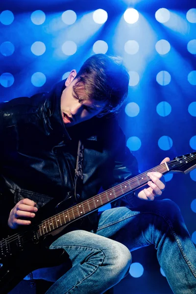 Jovem músico de rock atraente tocando guitarra elétrica e cantando. Estrela de rock no fundo dos holofotes — Fotografia de Stock