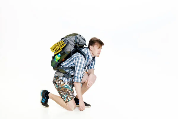 Young tourist with backpack ties up shoelaces on white background — Stock Photo, Image