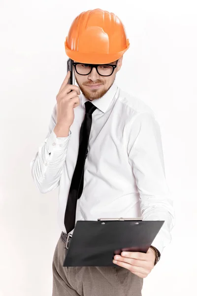 Νεαρός πολιτικός μηχανικός με πορτοκαλί κράνος με φάκελο μιλάμε στο τηλέφωνο σε λευκό φόντο — Φωτογραφία Αρχείου