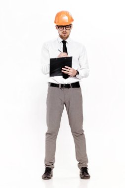 Genç inşaat mühendisi turuncu kask içinde klasöründe beyaz arka plan üzerinde yazıyor.