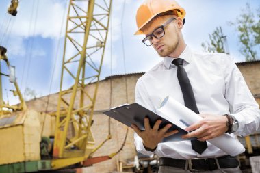 Mühendis Oluşturucu bir kask içinde çizimler inşaat alanında tutar.