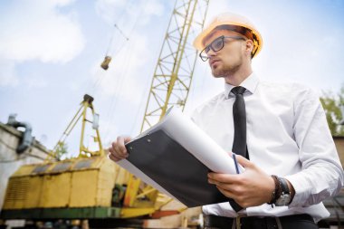 Mühendis Oluşturucu bir kask içinde çizimler inşaat alanında tutar.