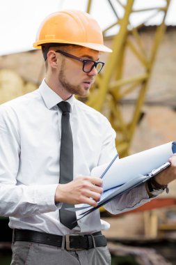 Mühendis Oluşturucu bir kask içinde çizimler inşaat alanında tutar.