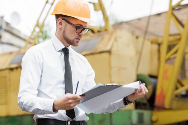 Mühendis Oluşturucu bir kask içinde çizimler inşaat alanında tutar.