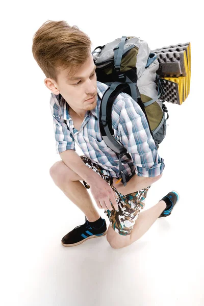 Young tourist is sitting with backpack on white background. traveler is preparing for hike — Stock Photo, Image