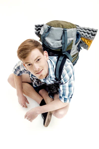 Funny Young tourist is sitting with backpack on white background. traveler is preparing for hike — Stock Photo, Image