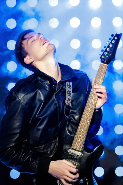 Young attractive rock musician playing electric guitar and singing. Rock star on background of spotlights — Stock Photo, Image