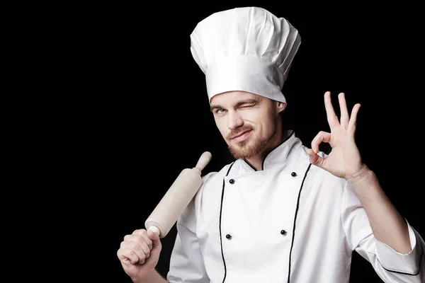Jeune homme barbu chef en uniforme blanc tient rouleau à pâtisserie sur fond noir — Photo