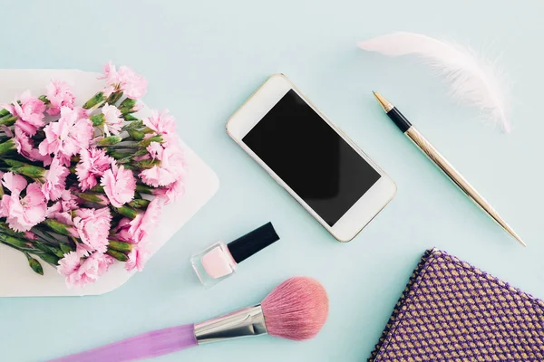 feminine flat lay on blue background, top view of womans desktop with  envelope, flowers, pen,  notepad and smartphone. mock up