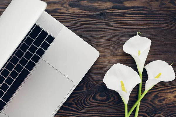 Flat lay branco calla flores e laptop no fundo de madeira, vista superior . — Fotografia de Stock