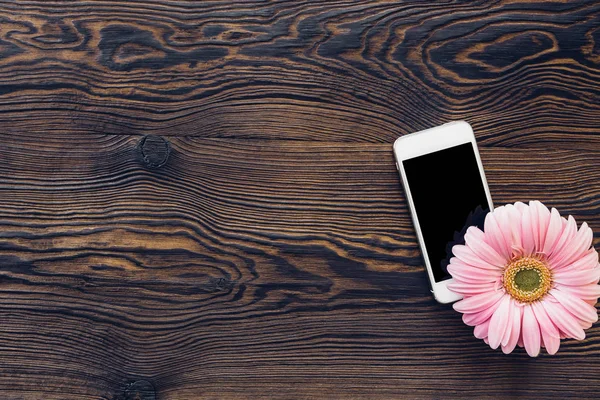 Λουλούδι και κινητό τηλέφωνο με κενή οθόνη για ξύλινο υπόβαθρο, το top view. mock πάνω — Φωτογραφία Αρχείου
