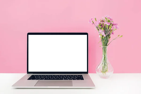 ラップトップ白い空白の画面とピンク色の背景上のテーブルの上に花瓶に花。モックアップします。 — ストック写真