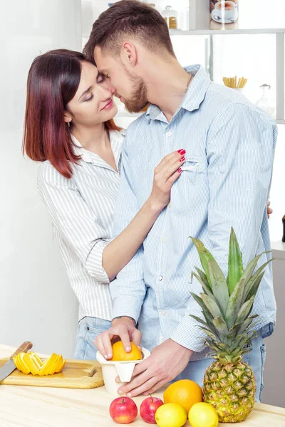 Pareja feliz en el amor en la cocina haciendo jugo saludable de naranja fresca. pareja es besos — Foto de Stock