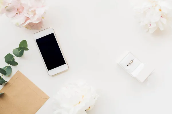 Ehering in weißer Geschenkbox auf Hintergrund von Blumen und Telefon. Ansicht von oben — Stockfoto