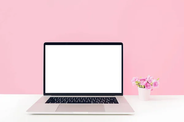 Laptop dengan layar putih kosong dan bunga di vas di atas meja pada latar belakang merah muda. pura-pura — Stok Foto