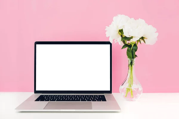 Laptop com tela branca em branco e flores em vaso na mesa sobre fundo rosa. Mock up — Fotografia de Stock