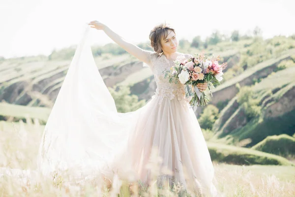 Bellas artes fotografía de boda. Hermosa novia con ramo y vestido con tren en la naturaleza — Foto de Stock