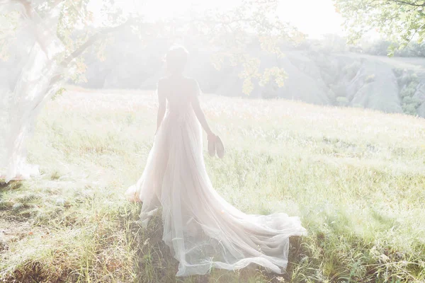 Fine Art Hochzeitsfotografie. schöne Braut mit Schuhen und Kleid mit Schleppe gegen die Sonne in der Natur — Stockfoto