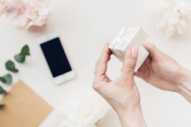 Eller arka plan üzerinde beyaz hediye kutusu çiçek ve telefon tutun. Üstten Görünüm