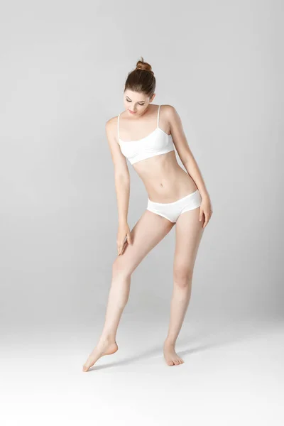 Smal vacker kvinna med perfekt kropp i vita underkläder på grå bakgrund — Stockfoto